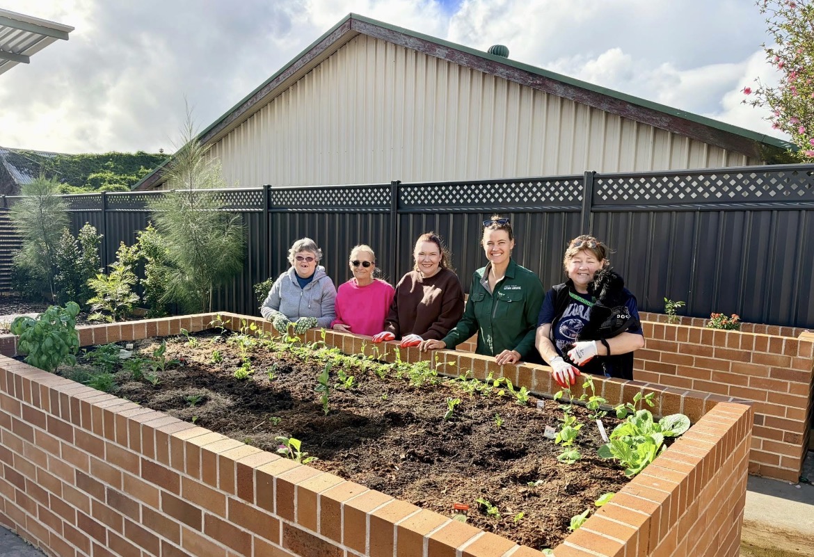 Group of community gardeners smiling behind a freshly planted brick raised bed
