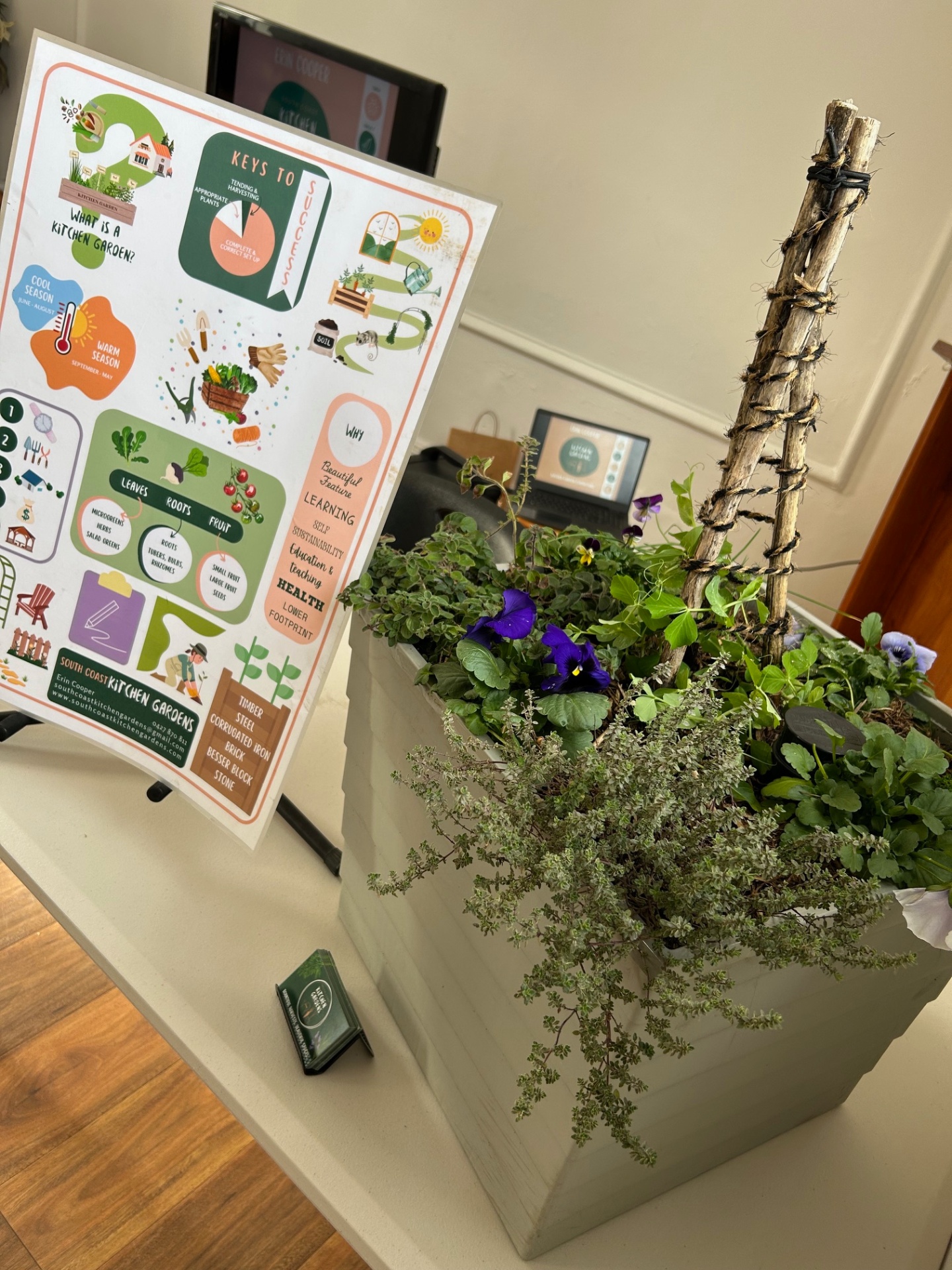 Workshop display planter with herbs, violas and a twine-wrapped trellis beside a kitchen garden info poster